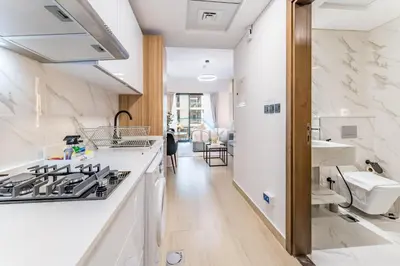 a kitchen with white counters and a stove top oven at Pool and Community View Studio with Balcony Near Park, Pantheon Elysee III, Jumeirah Village Circle by Deluxe Holiday Homes in Dubai