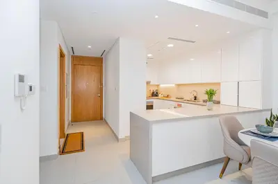 a white kitchen with a counter and a table at Escape24 Elegant 2BR with Canal view near Safa Park in Dubai