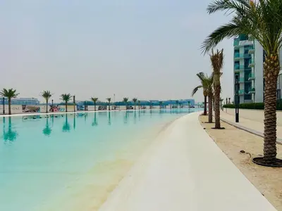 a swimming pool with palm trees next to a building at Luxurious 1 BR in District One Beach Access in Dubai