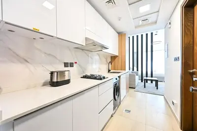 a white kitchen with white cabinets and a stove at Chic Studio in Prime JVC Spot - Holiday Boulevard in Dubai