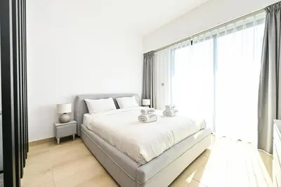 a white bedroom with a bed and a large window at Chic Studio in Prime JVC Spot - Holiday Boulevard in Dubai