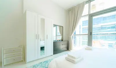 a white bedroom with a dresser and a large window at AWS Holiday Homes - Charming stay near Golf Course in Dubai