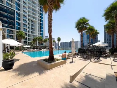 a man sitting next to a swimming pool with palm trees at Luxury Canal-View Stay in Damac Privee in Dubai