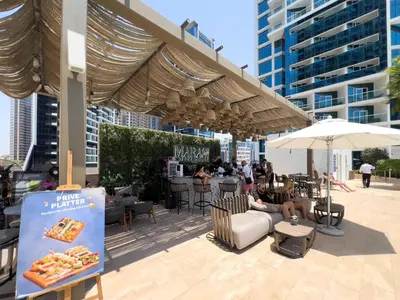 a man sitting in a chair under an umbrella on a patio at Luxury Canal-View Stay in Damac Privee in Dubai