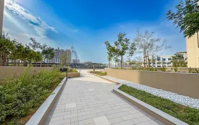 a walkway in a park with trees and buildings at Vogue Madinat Jumeirah Living Jadeel near Burj AlArab, One-Bedroom Apartment with Large Balcony and Pool View, Access to All Amenities in Dubai