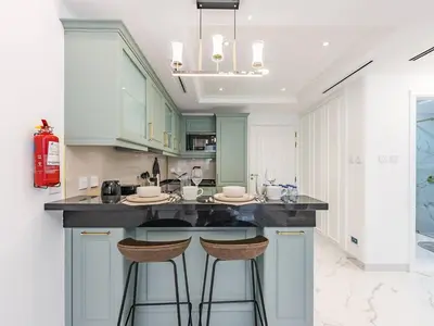 a kitchen with white cabinets and bar stools at Arjan 1BR Near Miracle Garden Pool & Parking in Dubai