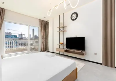 a white bedroom with a large window and a tv at Burj View - Luxury Studio - Near Dubai Miracle & Butterfly Garden- Arjan, Dubailand in Dubai