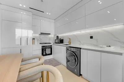 a white kitchen with a washing machine and a table at 1 Bedroom in Binghatti Lavender in Dubai