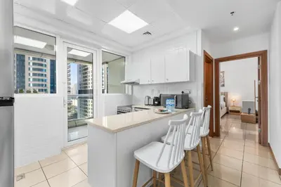 a kitchen with white cabinets and bar stools at Stylish 1BR in Marina, Balcony Near JBR in Dubai