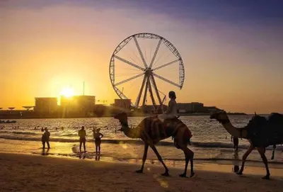 two people riding camels on the beach with a ferris wheel at Single Bed In Twin Room With Balcony For Female Guests Only in Dubai