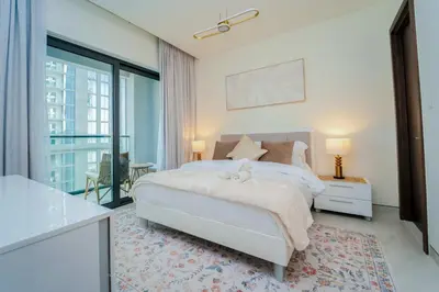 a white bedroom with a bed and a balcony at Luxury 1BR Suite - Comfort Meets Class in Dubai
