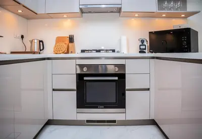 a kitchen with white cabinets and a black oven at Luxury 1BR Suite - Comfort Meets Class in Dubai