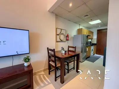 a living room with a table and a projection screen at Rare Holiday Homes - Near Miracle Garden - Dubai Sports City - Elite Residence - R1108 in Dubai