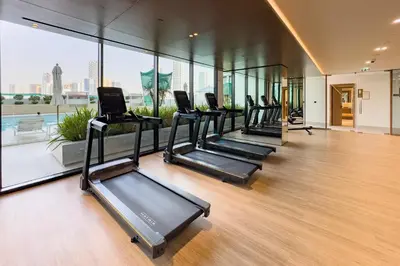 a row of treadmills in a gym with windows at Community Views 1BR Next to Mall and Park, Binghatti Amber, Jumeirah Village Circle by Deluxe Holiday Homes in Dubai