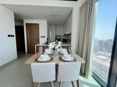 a dining room table with white chairs and a large window at Relax In Style 1br Haven In Binghatti Venus! in Dubai