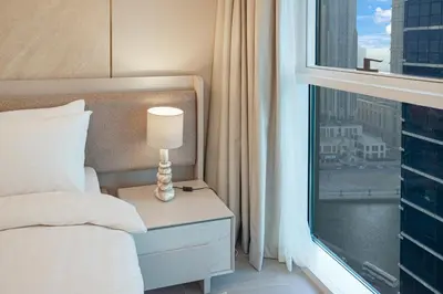 a bed with a lamp on a nightstand next to a window at 26- Apartment in Business Bay Dubai with Balcony & Pool in Dubai