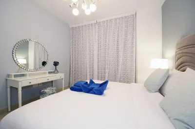a white bedroom with a large bed and a mirror at Stylish 1BR plus study room with Queen bed in Dubai