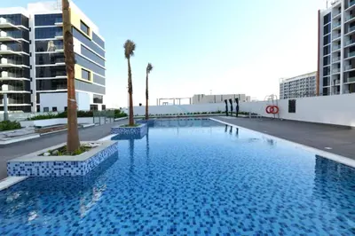 a large blue swimming pool with palm trees and buildings at Studio with Pool and Community View, Near Soho Garden DXB and Meydan Golf Club, Azizi Riviera 43, Al Merkadh by Deluxe Holiday Homes in Dubai