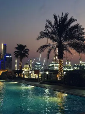 a pool with a palm tree and a city at night at Dubai Marina Modern 1 Bedroom Apartment - steps to tram & Marina Walk in Dubai