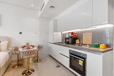 a white kitchen with a stove top oven next to a couch at LUX New Studio With 2 Double Beds in Downtown Dubai, Pool View, Free Parking in Dubai