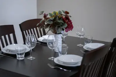 a table with plates and glasses and a vase of flowers at 1BR with Balcony View, Gym, Pool & Kids Play Area in Dubai