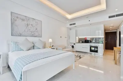 a white bedroom with a bed and a kitchen at Vibrant&Chic - Studio - 6MN Dubai Mall - Pool&Gym in Dubai