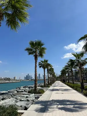 a sidewalk lined with palm trees next to the water at La Mer 1BR Ocean View 4 Pax in Dubai