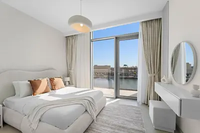 a white bedroom with a bed and a large window at 2BR Canal Front B3, Canal Views in Dubai