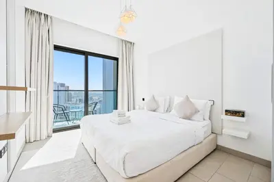 a white bedroom with a large bed and a balcony at High-Floor Luxury Spacious 1BR in Sobha Waves in Dubai