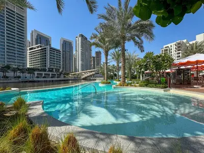 a large swimming pool with palm trees and buildings at Charming 1BR with Airy Terrace, Pool and Gym Access in Dubai