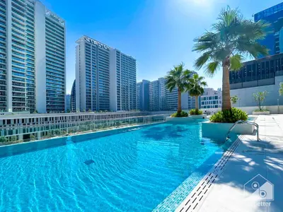 a large swimming pool with palm trees and buildings at Luxury at Sterling East Studio with Park Views in Dubai