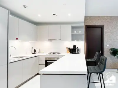 a white kitchen with white cabinets and a black chair at Modern 2B Apartment with Pool Acess SOBHA CREEK in Dubai