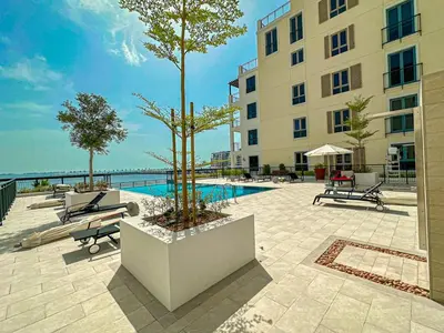 a building with a pool and two trees in a courtyard at HiGuests - Breezy 1 BR Retreat Near La Mer Beach in Dubai