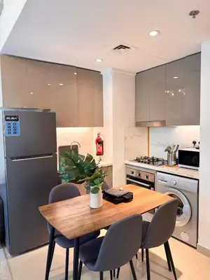 a kitchen with a wooden table and chairs and a refrigerator at COZY 1 BR Apartment in Dubai