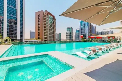 a swimming pool with chairs and an umbrella on a building at Vogue Downtown Mag 318 near Burj Khalifa and Dubai Mall, Studio Apartment with Balcony, Canal and City View, Access to all Amenities in Sabkhah