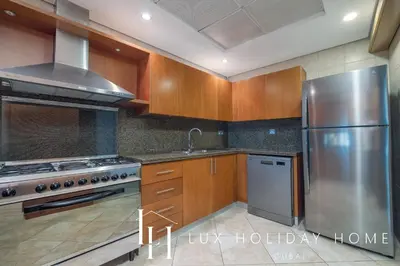 a kitchen with wooden cabinets and a stainless steel refrigerator at LUX The Luxury Sunny JBR Beach Views 2 in Dubai