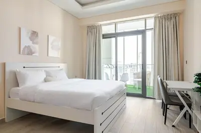 a white bedroom with a large bed and a desk at Cosy studio Free Parking Free unlimited drinkable water Near Downtown in Dubai