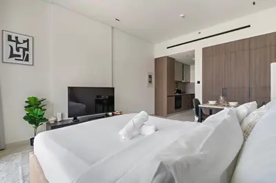 a white bedroom with a large white bed and a table at Chic Studio in Arjan with Gym Pool Free parking in Dubai