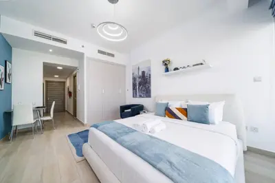 a white bedroom with a large bed and a table at Spacious JVC Studio Luxury Escape in Dubai
