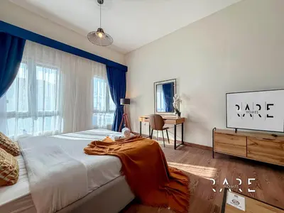 a bedroom with a large bed with blue curtains and a table at Rare Holiday Homes - Mediterranean Cluster - Near Metro - Discovery Garden - Building# Med 83 - R105 in Dubai
