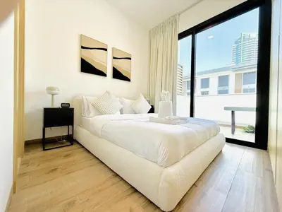 a white bedroom with a bed and a large window at Vserve - Peaceful 1 BR Getaway in Vibrant JVC in Dubai