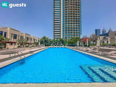 a large blue pool with chairs and a tall building at HiGuests - Luxe 2BR Overlooking Golf Course & Greenery in Dubai