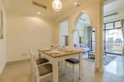 a white dining room with a table and chairs at Al Tajer Residence, Oldtown - 1BR Apartment - Allsopp & Allsopp in Dubai