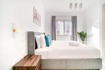 a white bedroom with a large bed and a wooden table at Stella Stays Barsha Heights in Dubai