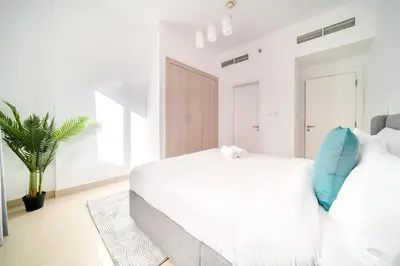 a white bedroom with a large white bed with blue pillows at Stella Stays Barsha Heights in Dubai