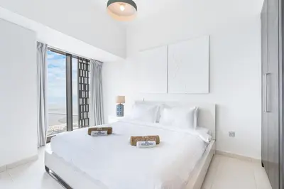 a white bedroom with a large white bed with a window at 44th Floor Home at Cayan Tower with Panoramic Views in Dubai