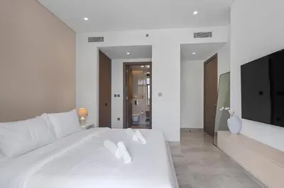 a white bedroom with a white bed and a television at Lavish 1-Bedroom with Burj Khalifa view in Peninsula in Dubai