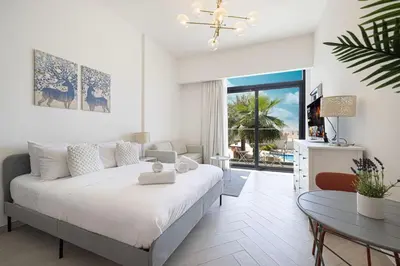a white bedroom with a bed and a table at Restay Homes - Chic Studio in JVC - Pool Views in Dubai