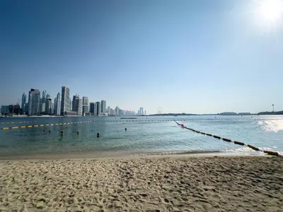 a beach with people in the water and a city at Palm Jumeirah Beachfront 1 Bedroom Apartment with Rooftop Infinity Pool and Atlantis Views in Dubai
