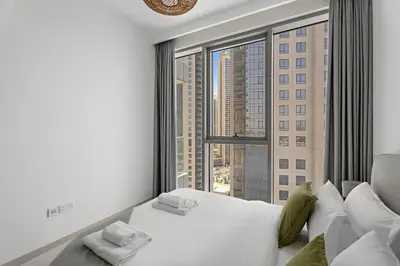 a bedroom with a white bed and a large window at Vayk - Bright & Elegant 2BR Apartment with Creek Views in Dubai